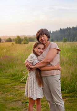 Grandmother and granddaughter hugging each other in the field at sunset.