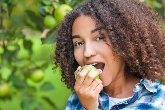 Outdoor portrait of beautiful happy mixed race African American girl teenager female child eating an organic green apple and smiling with perfect teeth
