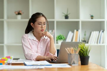 Cropped image of asian businesswoman analyzing paperwork using laptop to actively search for information tense expressions at the office.