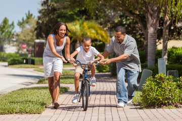 A young African American family with boy child riding his bicycle and his happy excited parents giving encouragement next to him