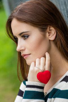 Beautiful thoughtful sad heartbroken girl or young woman with red hair holding a red heart necklace