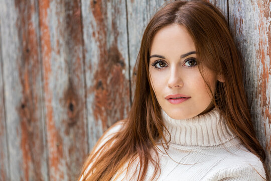 Outdoor portrait of beautiful girl or young woman with red hair wearing a white jumper
