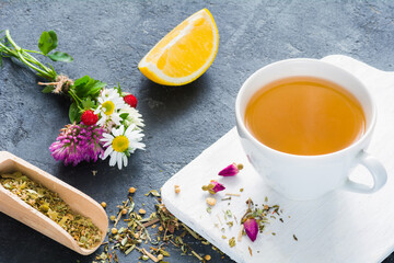 Cup of herbal green tea, lemon wedge, dry herbal tea, rose buds and bouquet of flowers. Concept of antioxidant beverage, healthy lifestyle, dieting, well-being