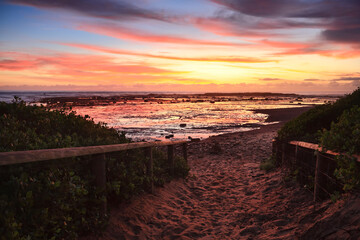 A sandy path to the beach as dawn skies aglow with vibrant colour before the sunrise.  Northern Beaches, Sydney, Australia