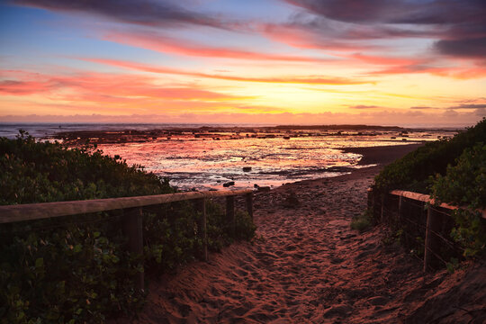 A sandy path to the beach as dawn skies aglow with vibrant colour before the sunrise. Northern Beaches, Sydney, Australia © Designpics
