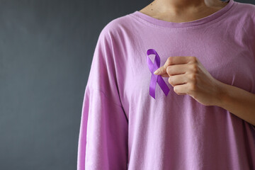 Close up of a slim woman in purple t-shirt holding and showing purple awareness ribbon. Symbol is...