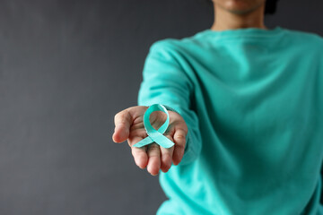 Female in green sweater holding and showing green organ transplant awareness ribbon to the camera,...