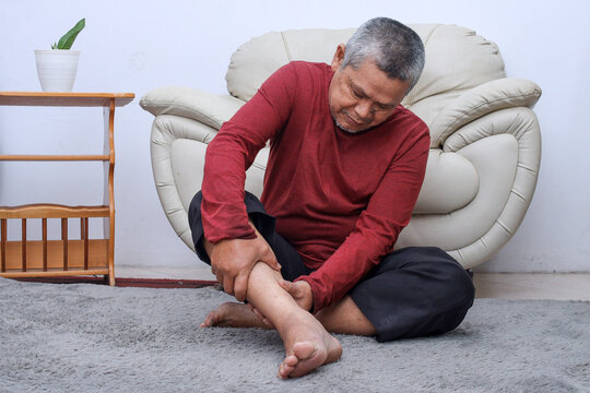 Senior man sitting on floor have cramps in his calves, massage the calf by hands.