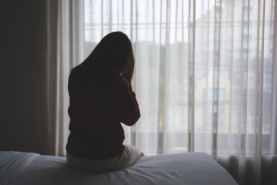 Silhouette of a woman sitting and crying on a bed in bedroom