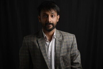 Portrait of happy corporate dressed up person in suit and wearing specs portraying different moods. Low key shoot of bearded office man well suited. Black background.
