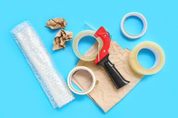 Adhesive tape rolls, dispenser, bubble wrap and paper on blue background