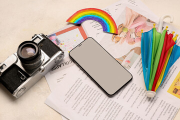 Mobile phone with photo camera, rainbow, umbrella and newspapers on grunge background. Weather...