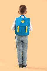 Little schoolboy with blue backpack on orange background, back view