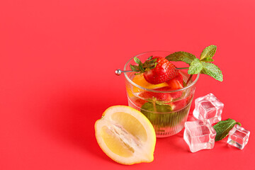 Glass of fresh lemonade with strawberry and lemon on red background