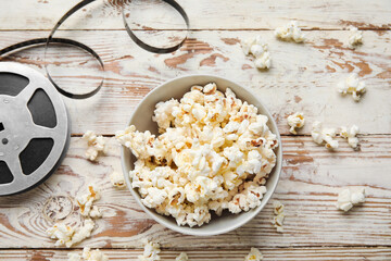 Bowl with tasty popcorn and film reel on white wooden background