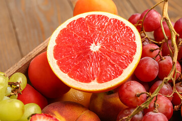 Box with different fresh fruits on wooden background, closeup