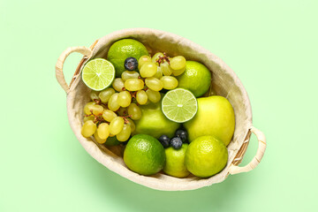 Wicker basket with different fresh fruits on green background