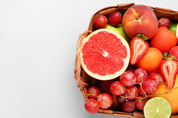 Wicker basket with different fresh fruits on grey background