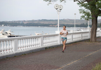 The concept of running, fitness, sports, training and a healthy lifestyle, weight loss - a running girl along the promenade by the sea