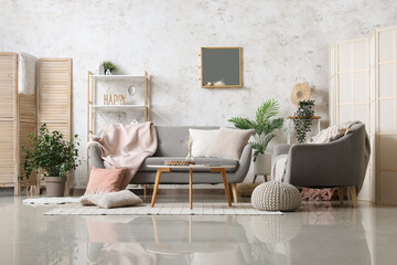 Interior of light living room with cozy grey sofa, armchair and mirror