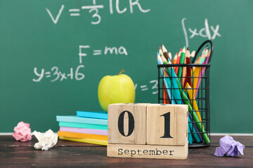 Different stationery, fresh apple and calendar with date SEPTEMBER 1 on wooden table against green...