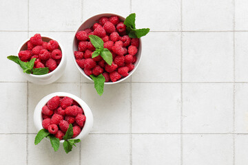 Bowls with fresh raspberries and mint on white tile background