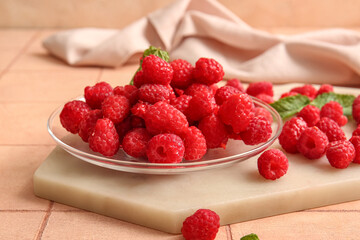 Glass plate with fresh raspberries and mint on pink tile table