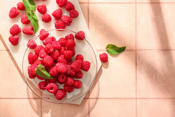 Glass plate with fresh raspberries and mint on pink tile table