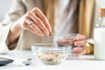 Healthy eating at work as a woman creates a nourishing bowl of muesli, enriched with almonds and hazelnuts. This photo captures the essence of balanced nutrition and workplace wellness.  