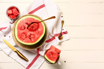 Half of fresh watermelon and cups with pieces on white wooden background