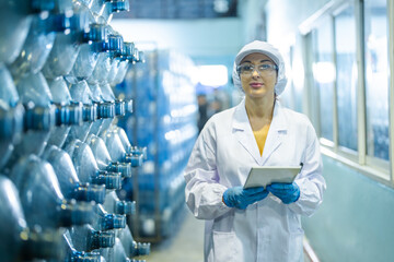 Factory worker checking water bottles in the warehouse at the industrial factory. Female worker recording data at the beverages manufacturing line production.