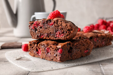 Board with pieces of raspberry chocolate brownie on grey tile table