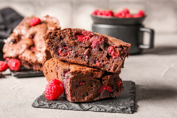 Board with pieces of raspberry chocolate brownie on grey table