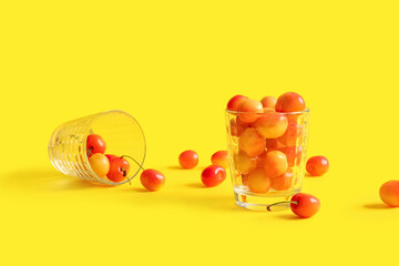 Cups with sweet yellow cherries on yellow background