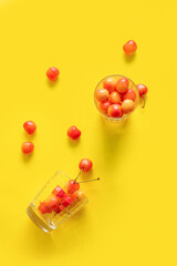 Cups with sweet yellow cherries on yellow background