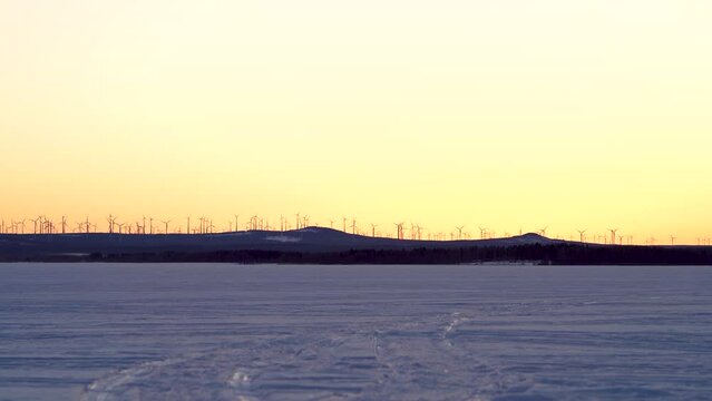 Markbygden Windmill park in the distance with Wind Turbines in motion rotating generating green electricity at sundown on a hill outside of Pitea, Northern Sweden. 
