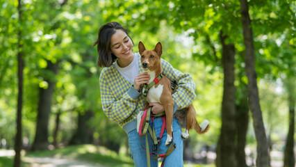 Fototapeta premium A young beautiful woman holds a dog in her arms for a walk. non-barking african basenji dog. 