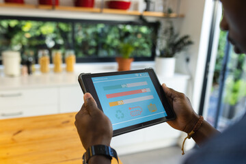 African american man using tablet with smart home interface in kitchen at home
