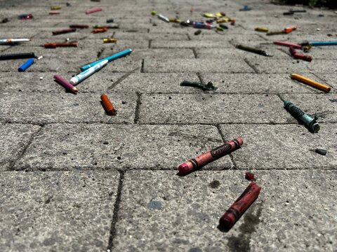 Colori a cera per bambini, sparsi su un marciapiede mattonellato con piastrelle grige
