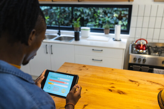 African american man using tablet with smart home interface in kitchen at home