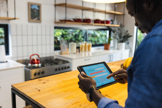 African american man using tablet with smart home interface in kitchen at home