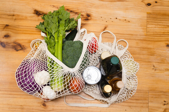 Overhead view of vegetables and spices in shopping bags on wooden table in kitchen