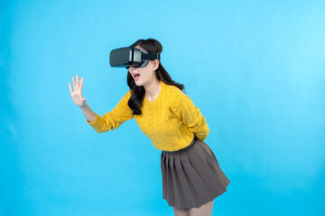 long haired asian woman Put on 3D VR glasses about the future of gaming and modern technology. hand to side wow and excited wearing a yellow coat and skirt Taking photos in the blue screen studio