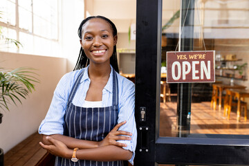 Portrait of happy african american female cafe owner in apron staying in front door