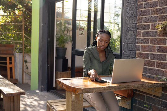 African american woman using laptop and smartphone outside a cafe
