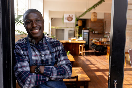 Portrait of happy african american male cafe owner in apron staying in front door