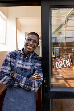 Portrait of happy african american male cafe owner in apron staying in front door