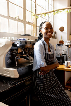 Portrait of happy african american female cafe owner in apron staying by coffee machine