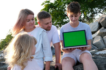 Fototapeta premium family holding a green screen laptop, and looking into it vacation beauty little girl adult boy man parents siblings children stones beach park happy