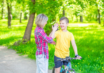 Mom and her young son give high five while cycling in the park
